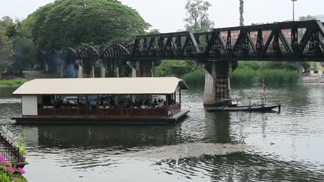 hd ferry with tourists travelling under the river kwai bridge in kanchanaburi, thailand