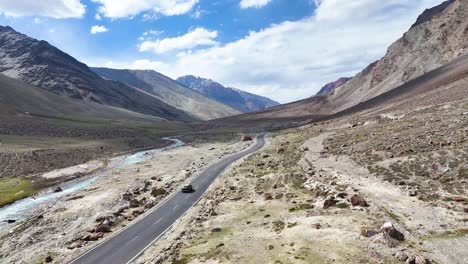 aerial drone shot of a lone car cruising down a long, straight highway cutting through ladakh’s rugged terrain.
