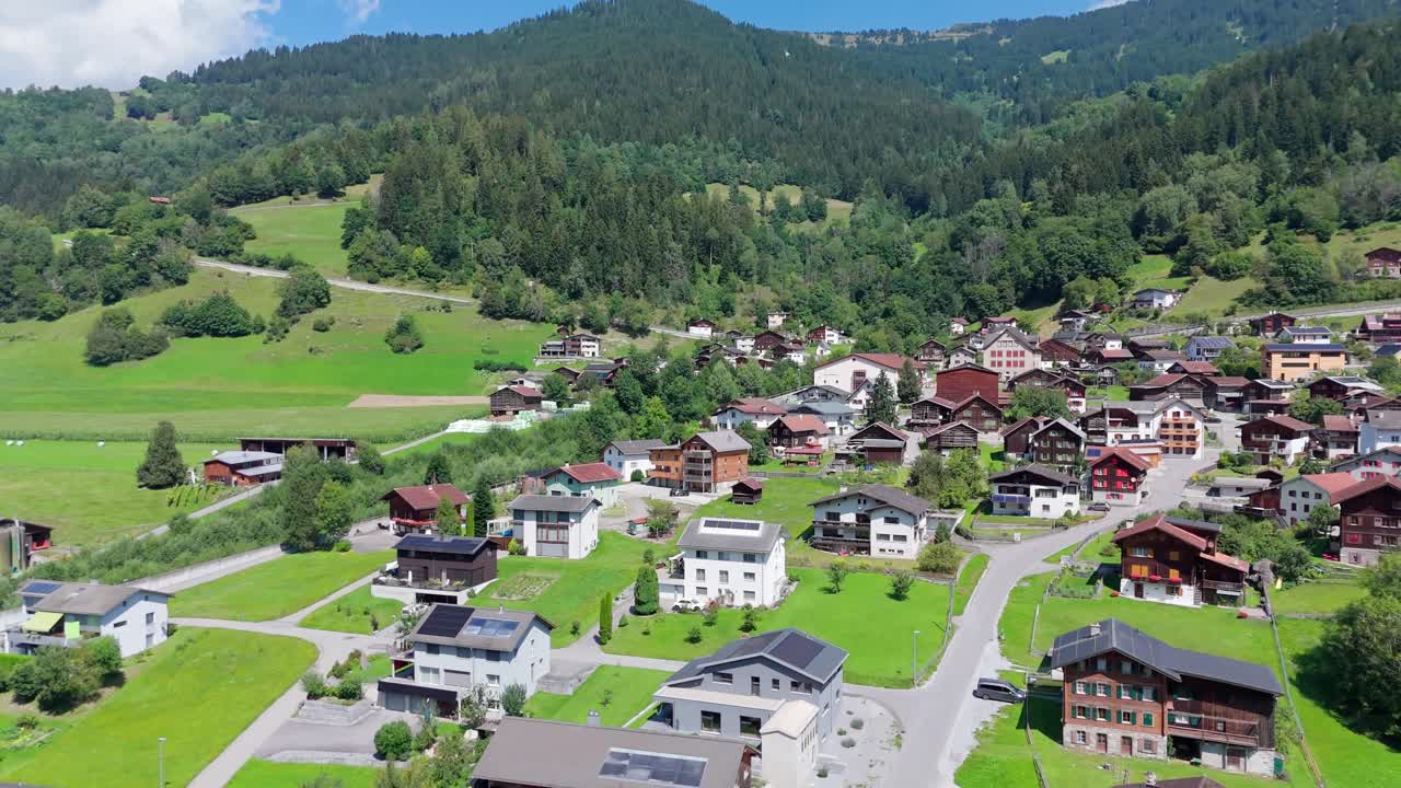 Picturesque Swiss village surrounded by lush green hills and forest. Mix of traditional wooden chalets and modern detached houses with solar panels. peaceful alpine landscape in summer. Aerial view