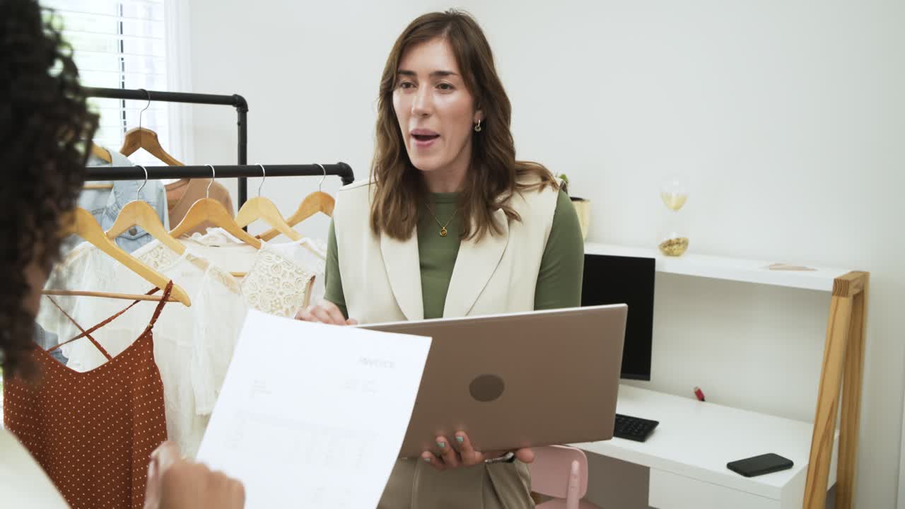 Diverse kvindelig duo vælger bluse efter at have læst formular og bruger bærbar computer i showroom, med plads til tekst.
