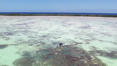 A-single-boat-on-a-clear-shallow-coral-reef,-sunny-day,-aerial-view