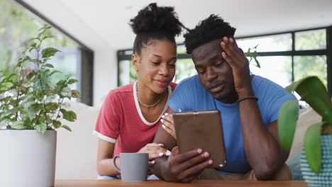 Video-of-happy-african-american-couple-sitting-on-sofa-and-using-tablet