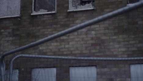 Dangerous-brick-building-with-metal-shutters-after-fire-surrounded-by-fencing-tilt-shot