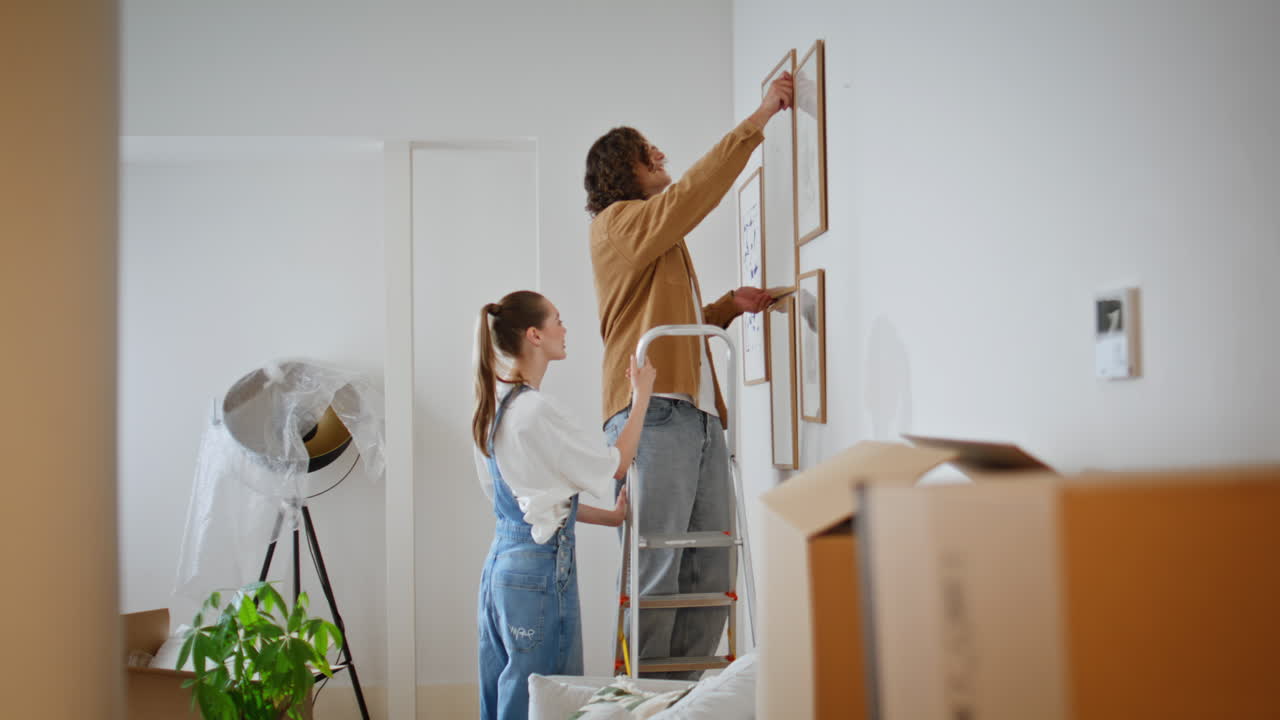 Spouses decorating new apartment with modern artworks. Young woman helping