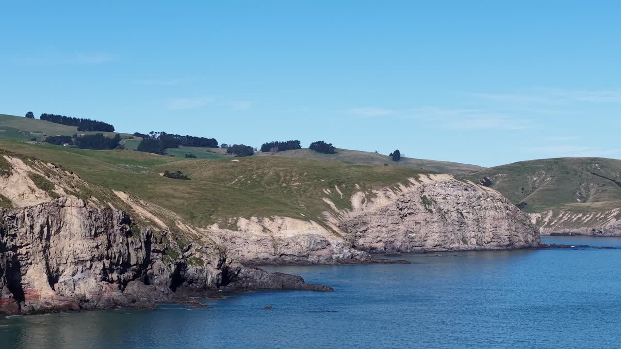 Zoomed in aerial reverse above beautiful inky-blue ocean showing volcanic rock details and farmland (Banks Peninsula South, New Zealand)