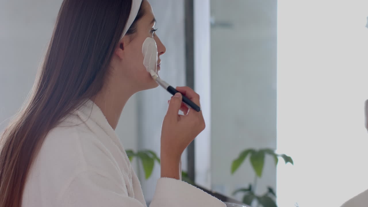Applying facial mask, woman in bathrobe enjoying spa treatment at home, copy space