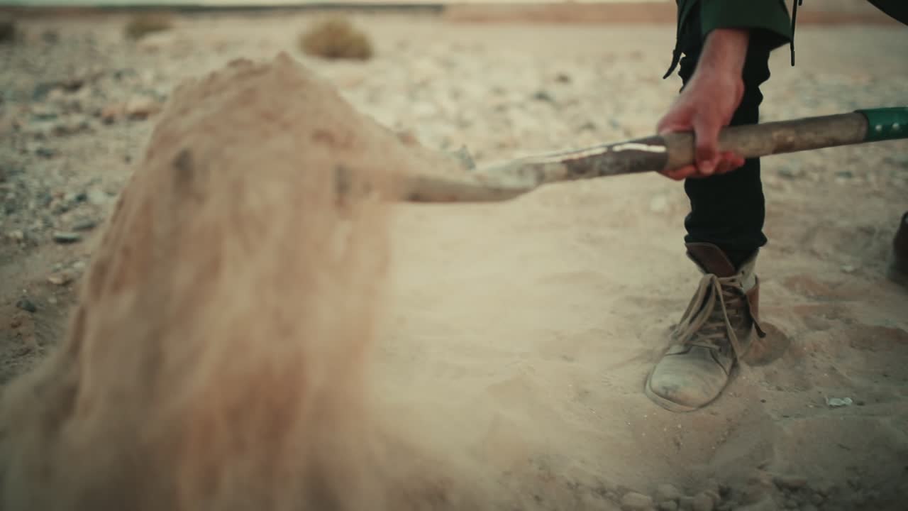 Man shovels dusty sandy soil in desert with spade, low angle slow motion