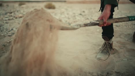 man shovels dusty sandy soil in desert with spade, low angle slow motion