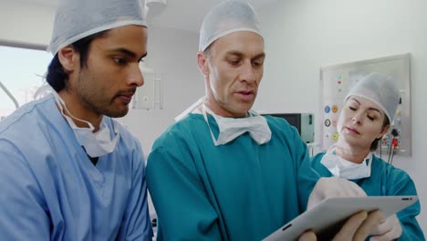 Surgeons-discussing-over-digital-tablet-in-operation-room