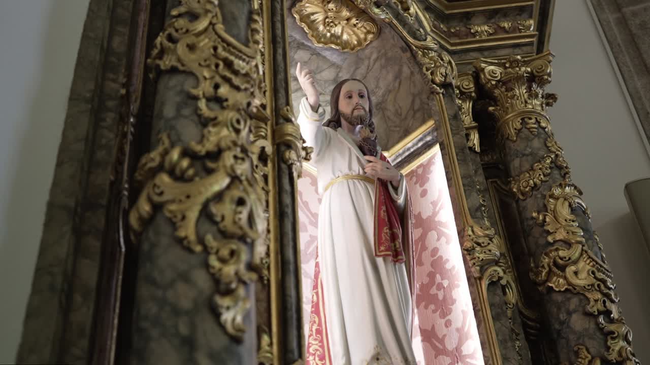 Estátua de Jesus com a mão levantada em uma alcova de igreja ornamentada em ouro e mármore