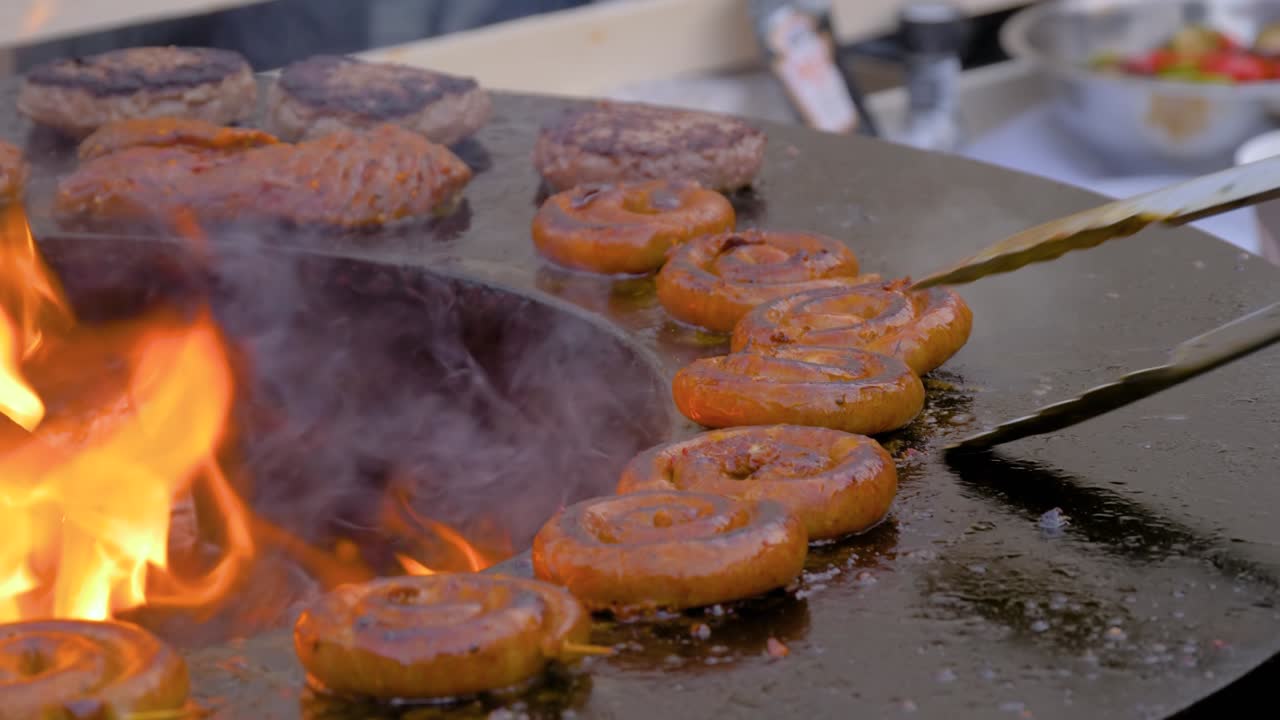 cámara lenta: chef asando salchichas de cerdo en espiral frescas en un brasero con llama caliente