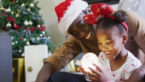 Glücklicher-Afroamerikanischer-Vater-Mit-Tochter,-Die-Mit-Schneekugel-Spielt