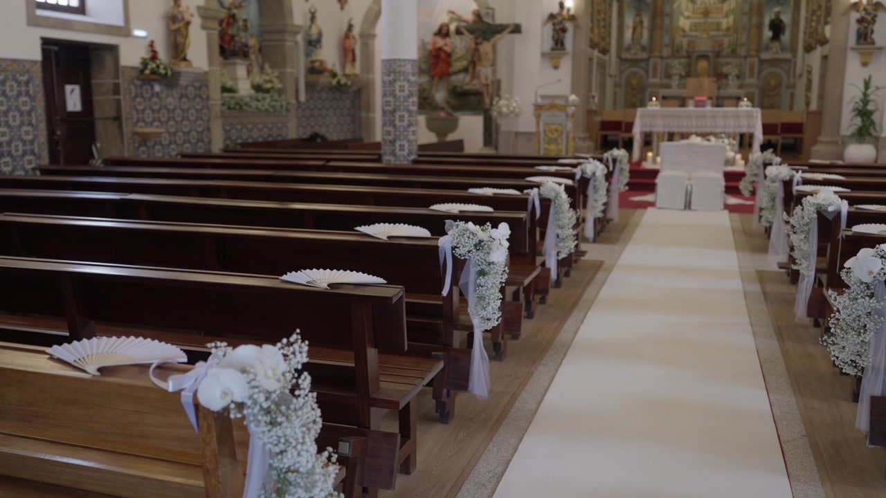 Navata della chiesa con panche in legno decorate con fiori bianchi, nastri e ventagli, in preparazione per una cerimonia nuziale