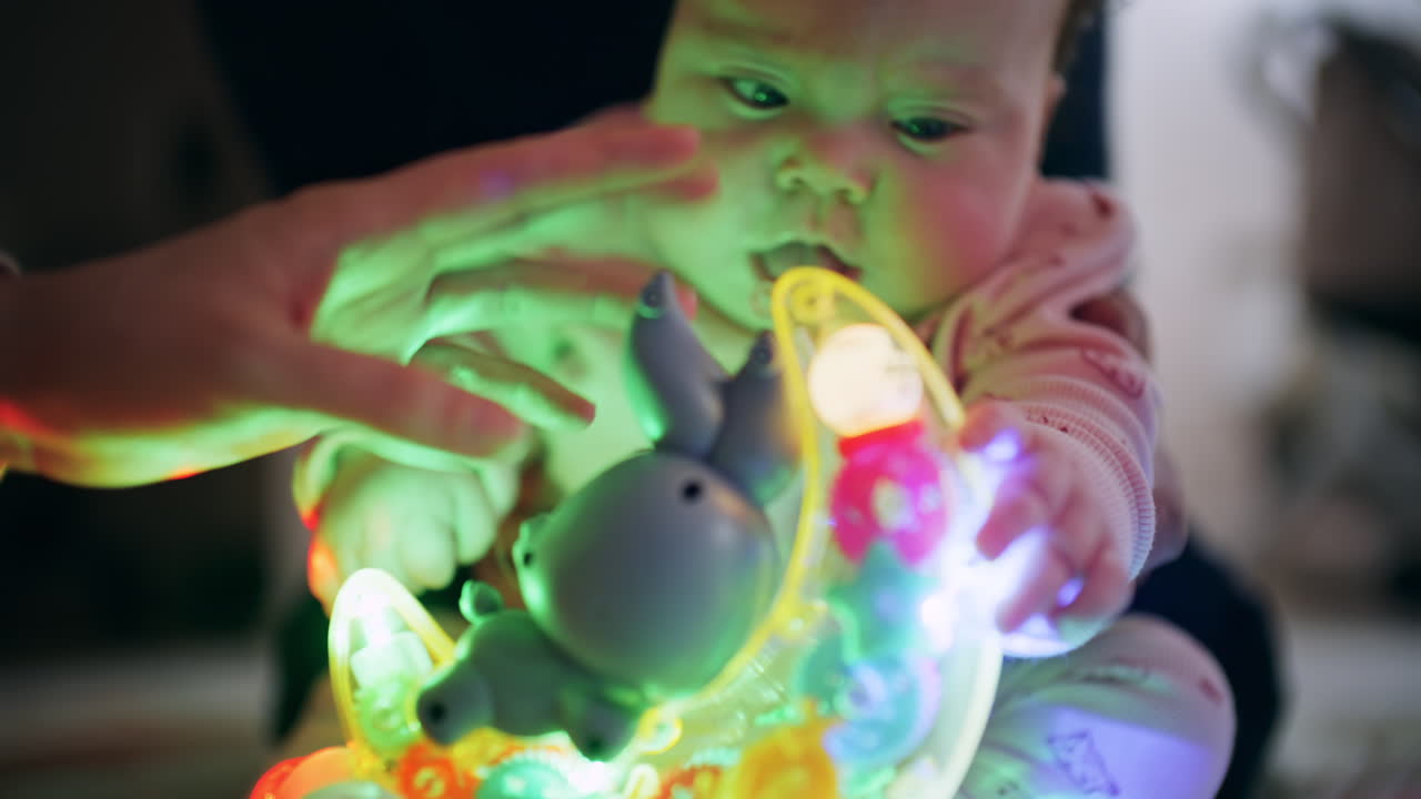 Bebê observando um brinquedo giratório com luzes brilhantes e coloridas durante a brincadeira com o cuidador.