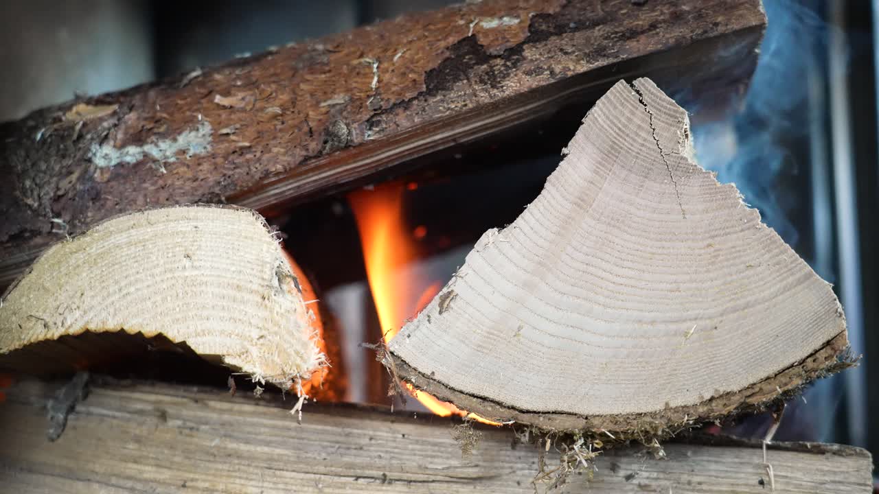 Bidikan Close-up Gerak Lambat Kayu Bakar Menyala dengan Serat Kayu Terlihat Jelas. Api Berkobar di Satu Sisi Sementara Asap Mengepul ke Atas di Sisi Lain, Menciptakan Pemandangan Api Dalam Ruangan yang Dramatis dan Penuh Suasana.