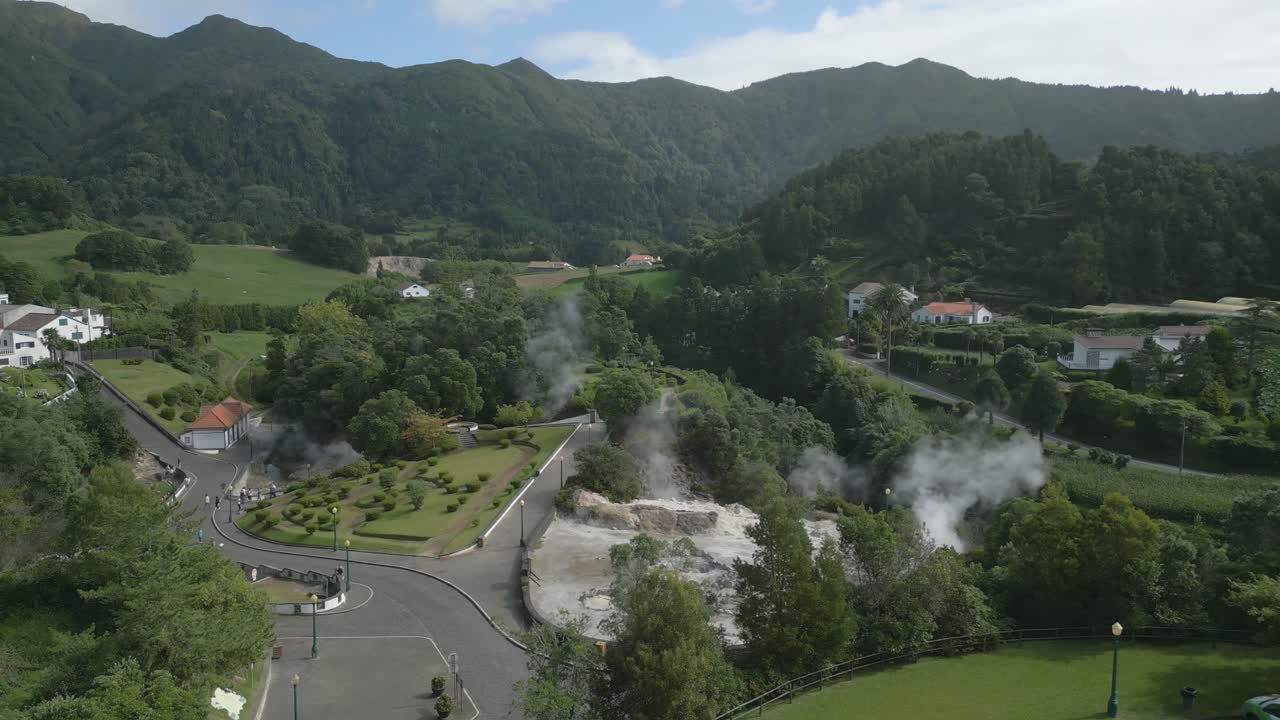 Steam rise from geothermal pools volcanic landscape, lush Furnas village. Aerial