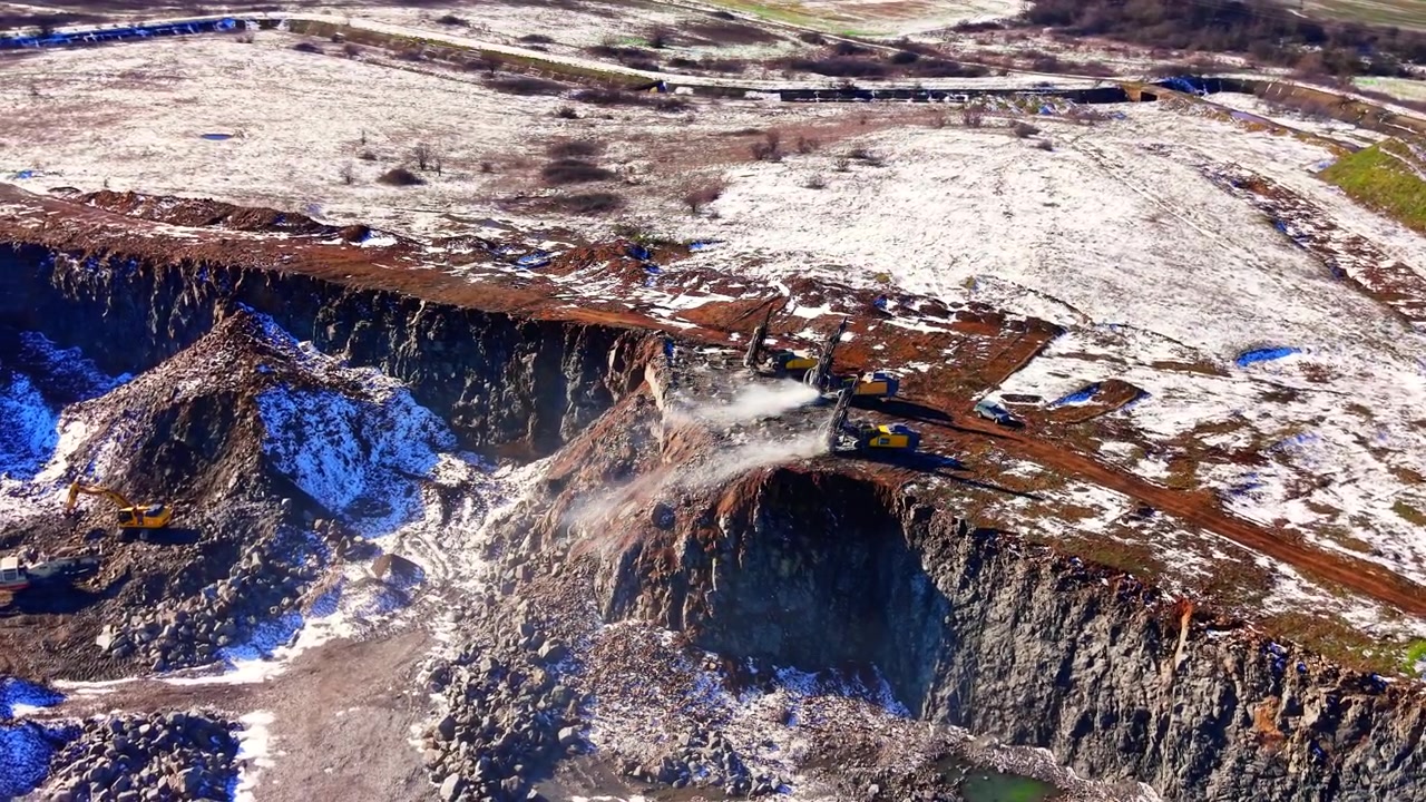Luftfoto av utgraving i steinbrudd, Bulgaria. Borerigg, gravemaskin og lastebil arbeider blant snøflekker og steinete klippevegger.