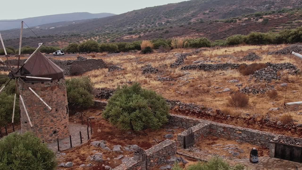 Mulini a vento tradizionali in pietra con pale rotanti in un paesaggio rurale arido