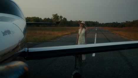 woman walking on the runway with a small airplane in the background at sunset