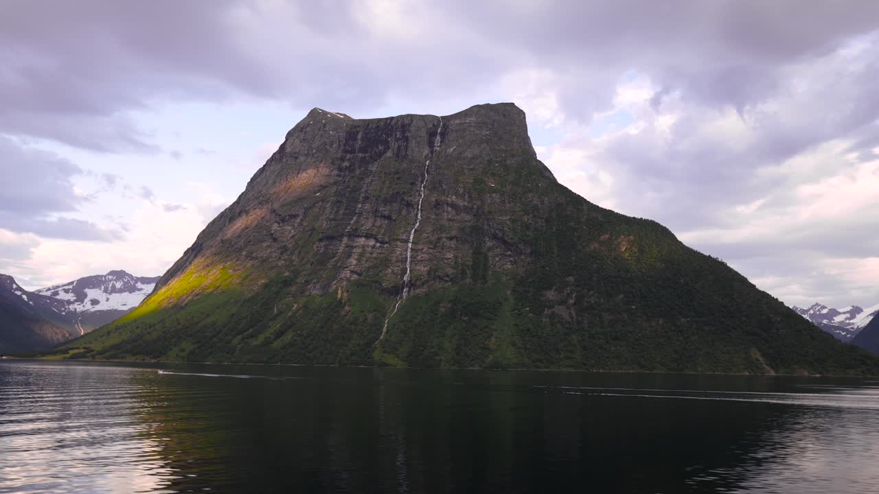 Beautiful scenery shot from the car, driving by a large mountain standing in a lake, cloudy blue sky in the background