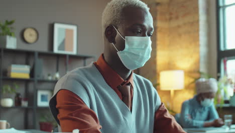 hombre de negocios afroamericano con máscara trabajando en una computadora portátil en la oficina