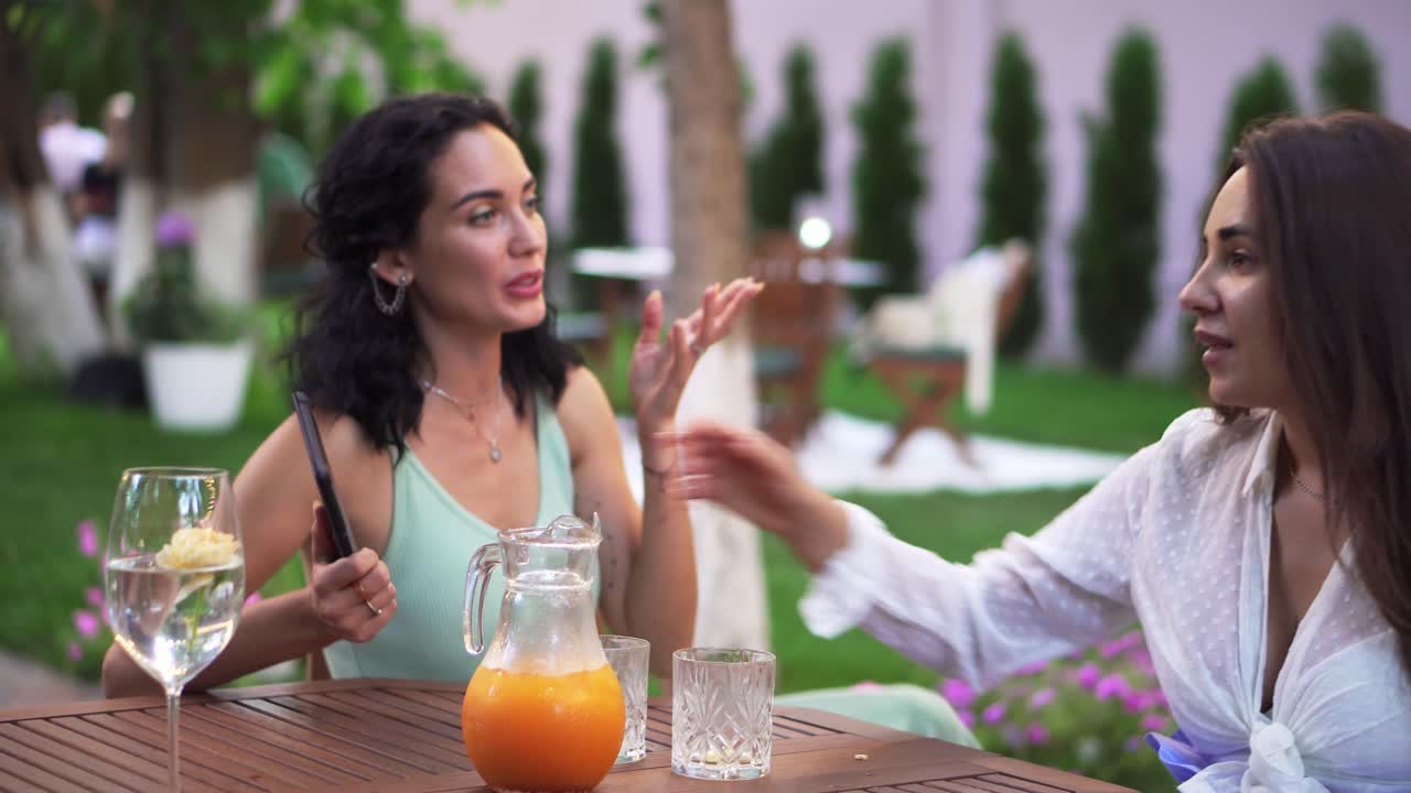 dos mujeres jóvenes emocionadas vinieron a sentarse a la mesa en un café al aire libre, charlando emocionalmente
