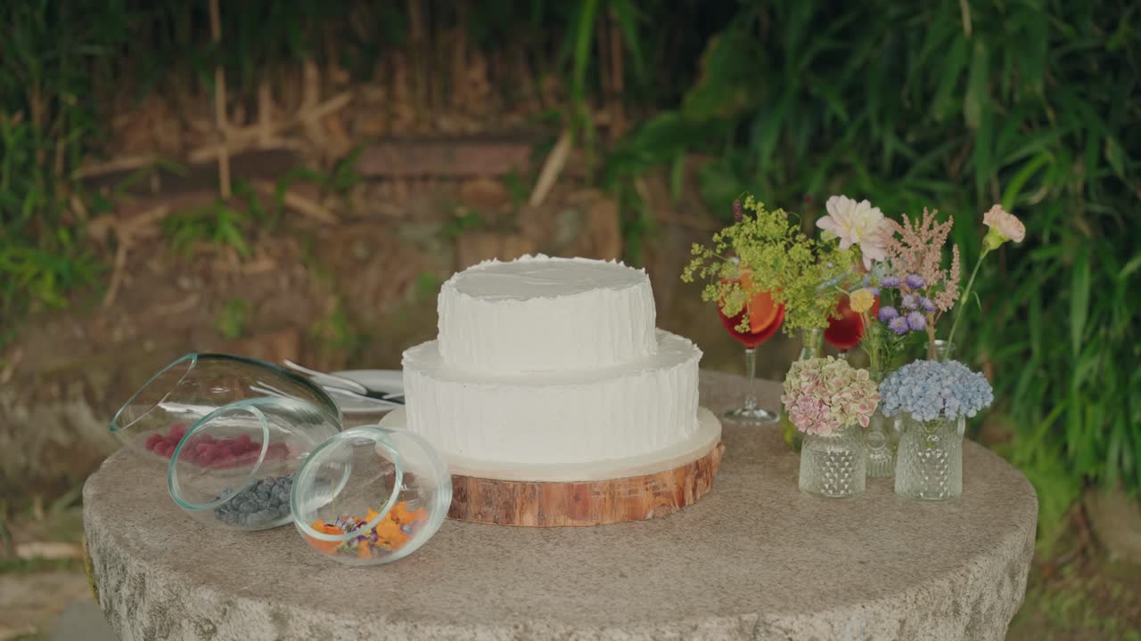 White wedding cake on rustic table with flowers and decor outdoors