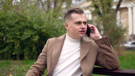elegant smiling man talking on the phone while sitting on a bench in the street