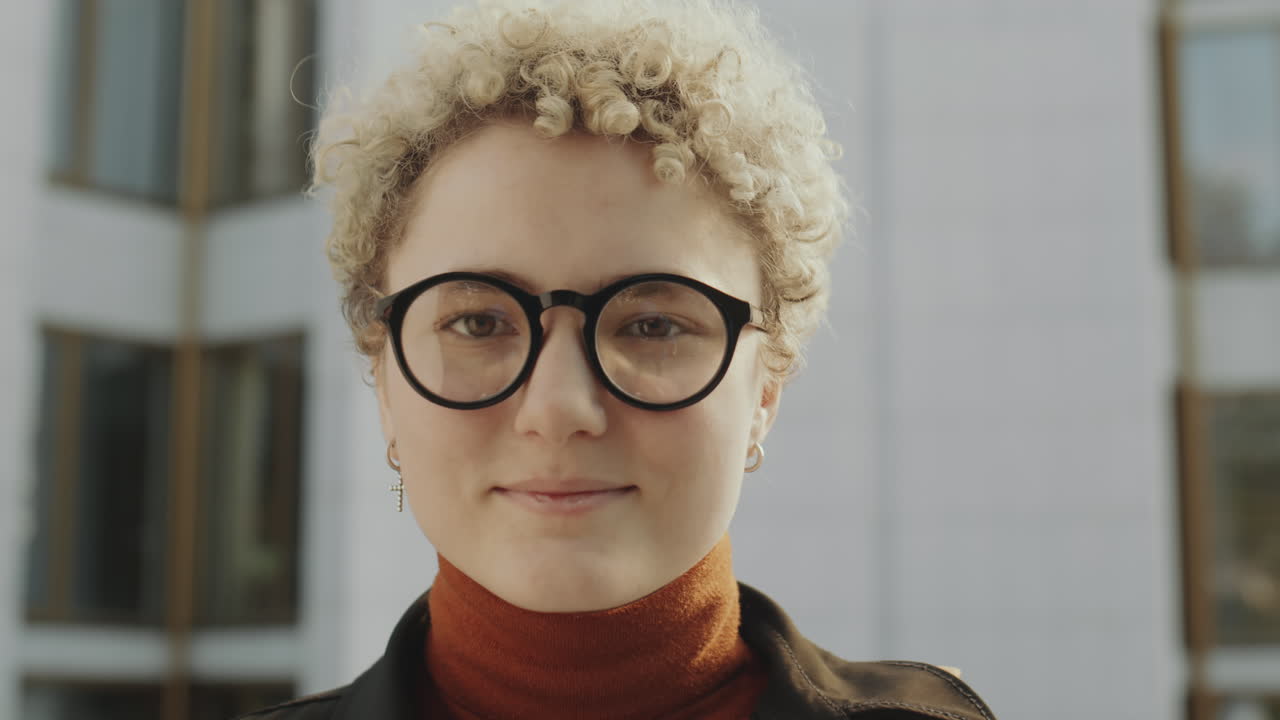 Close-up portrait of a young person with curly blonde hair and glasses