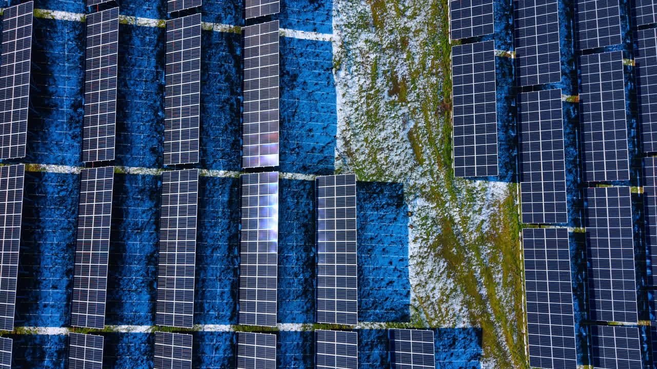 Motivo aereo di moduli fotovoltaici con chiazze di neve. Vista dall'alto di pannelli solari che evidenzia motivi geometrici, texture e chiazze di neve sciolta