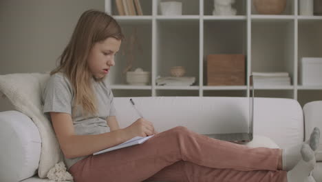 adolescente está escribiendo en el cuaderno sentado en casa en la sala de estar en el sofá el fin de semana relajarse en las vacaciones o el fin de semana