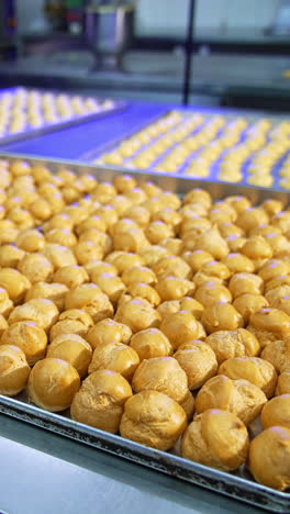 large metal tables covered with baking sheets full of baked éclairs. pastry prepared for stuffing with cream. food factory production. vertical video