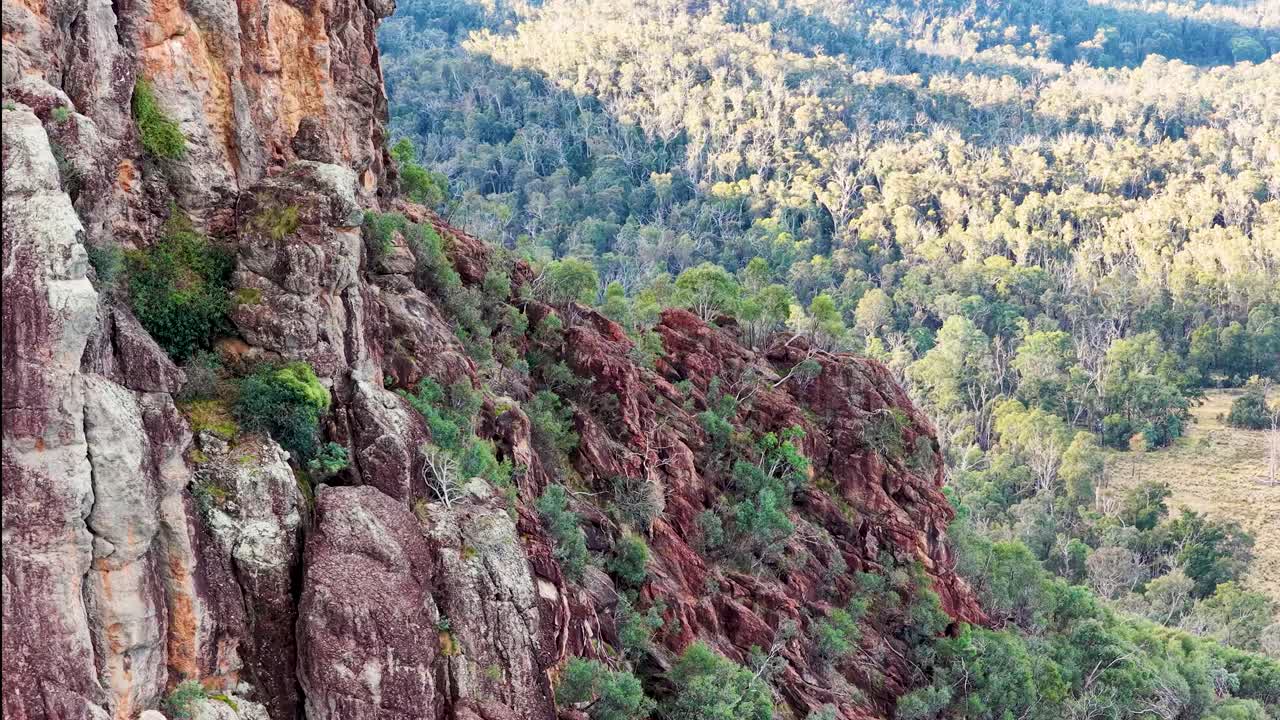 Drone pans Timor Rock’s rugged volcanic outcrop above dense bushland in soft sunset light