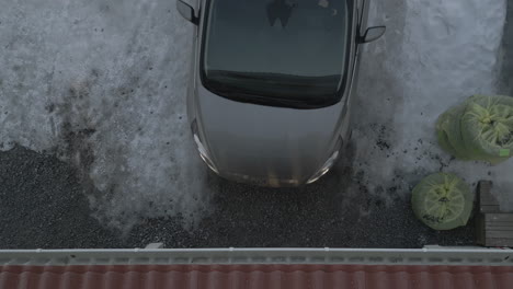 grey car reverses out of garage onto ice, top down aerial view