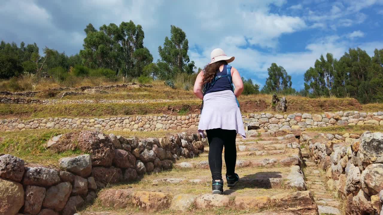 Close-up of a woman hiking up ancient Inca steps, revealing terraced ruins at Inkilltambo. Cusco, Peru, Qhapaq Ñan road system