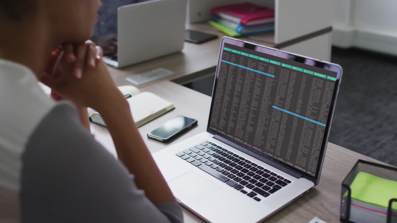 Mixed race woman sitting at desk watching coding data processing on laptop screen