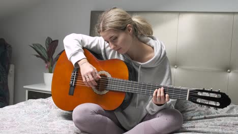 young woman playing acoustic guitar on bed