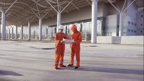 two construction workers in orange uniform and hardhats meeting each other at the bulding object and examining the constructed building together. teamwork concept