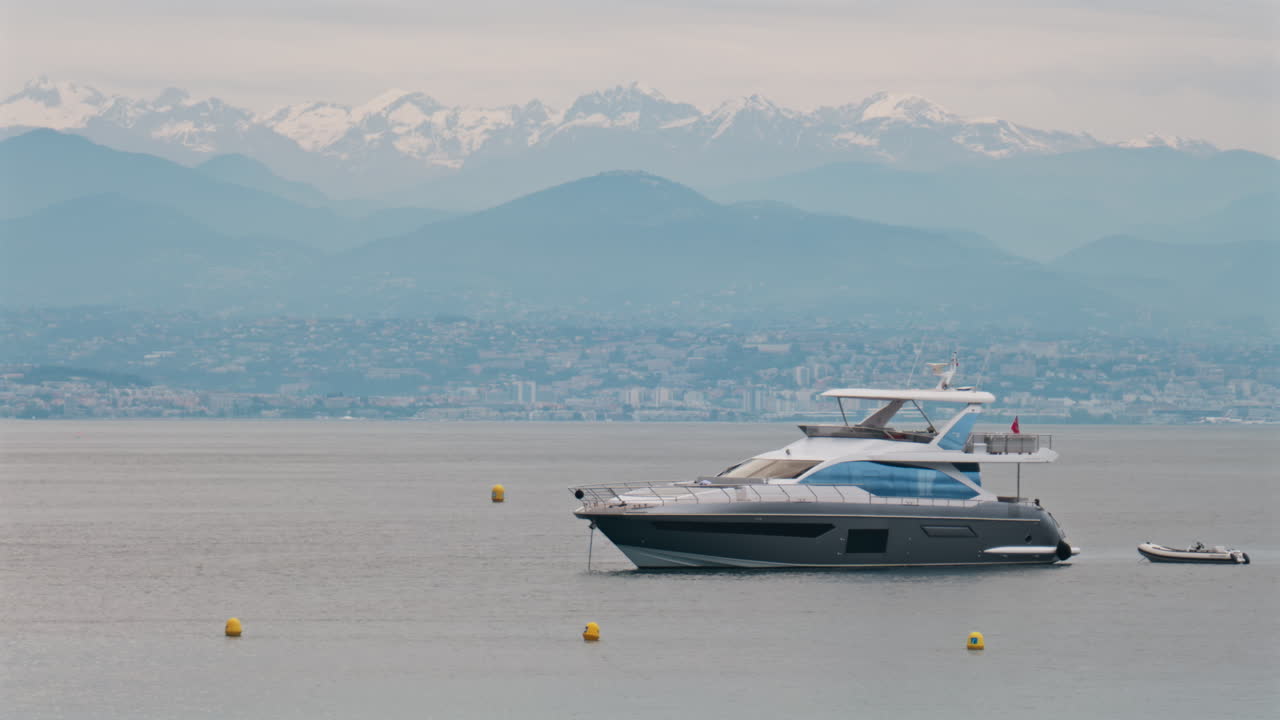 Antibes, Francia - 6 maggio 2025: persone su una barca ormeggiata in mare, con la città e le montagne sullo sfondo in pieno giorno