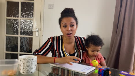 young woman with small child on business video call briefing others whilst looking directly to camera