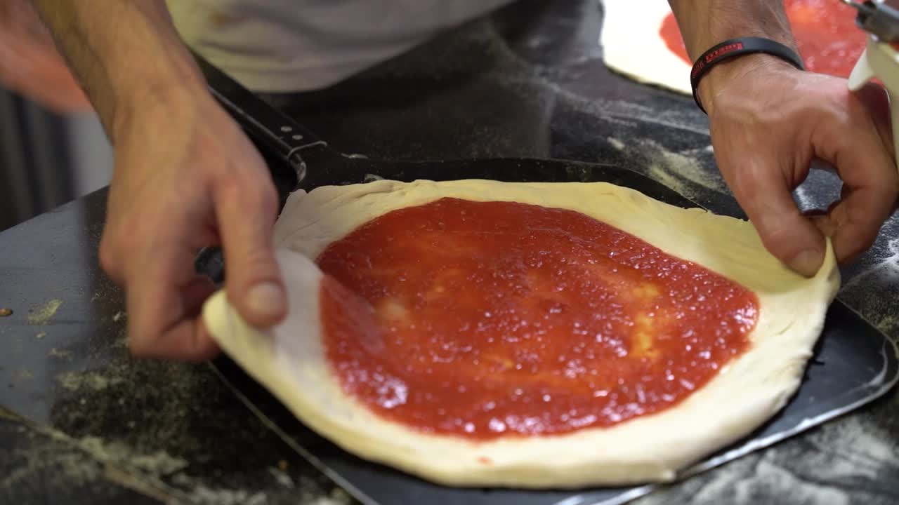 Un primo piano di mani che sistemano con cura l'impasto della pizza condito con salsa di pomodoro fresca. La scena cattura l'arte coinvolta nella creazione di una pizza autentica.
