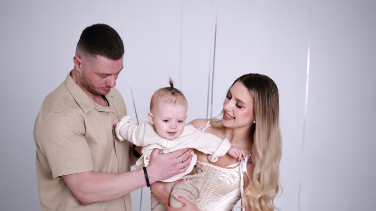 Long-haired blonde woman holding a beautiful active baby. Caucasian family portrait in studio. White backdrop.
