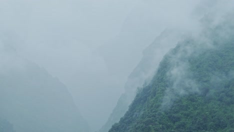 moody misty mountain background with copy space, blue layers of mist in a steep mountains valley background with copyspace with clouds moving from above the trees in an elevated aerial view