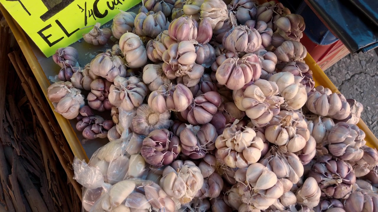 Primer plano de bulbos de ajo solo frescos expuestos para la venta en un mercado callejero tradicional, mostrando productos de cosecha local en un tianguis en México.