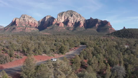 aerial: shot in sedona arizona of a car driving through rock formations and a beautiful landscape on a sunny day