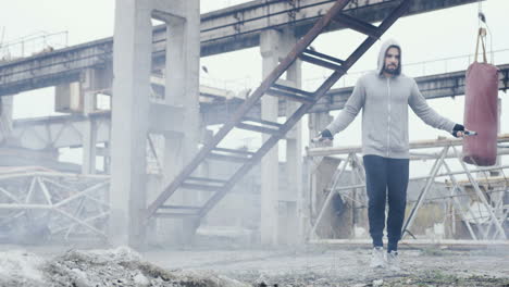 caucasian man with beard in a grey hoodie jumping rope outdoors an abandoned factory on a cloudy morning