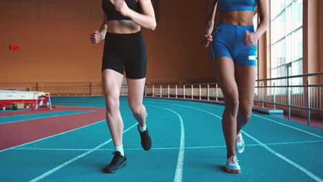 Zwei-Multiethnische-Sportlerinnen,-Die-Zusammen-Auf-Einer-Indoor-Bahn-Laufen-3