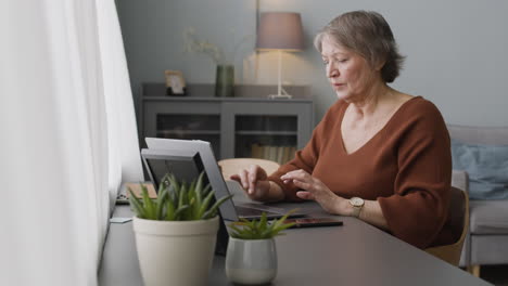 focused woman typewritting at laptop sitting at desk at home 2