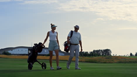 couple golf players discuss sport course outside. two golfers walk grass field.