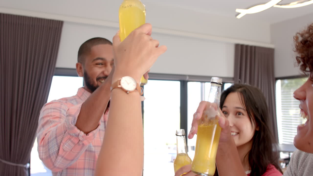 Diverse friends toasting with bottles of beer, enjoying time together indoors